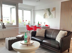 Ein modernes Wohnzimmer mit einer Ledersofa, einem runden Couchtisch und einem Essbereich mit roten Stühlen.