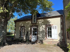 Ein zweistöckiges Gebäude mit Backsteinfassade, einem Schotterweg und einem großen Baum, der Schatten spendet.