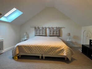 Ein Schlafzimmer mit schrägen Wänden, einem Bett mit gestepptem Kopfteil, zwei Nachttischlampen, einem Heizkörper und einem Oberlicht.