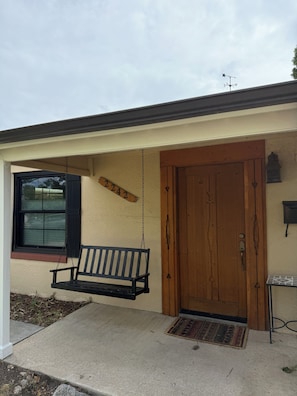 Uma casa com porta de madeira, um banco de balanço e uma caixa de correio.