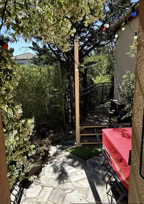 Ein überdachter Patio-Bereich mit einem roten Tisch, Steinböden und einer Pergola mit Lichterketten.