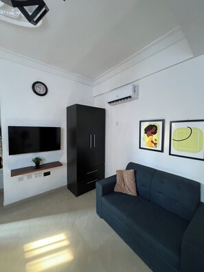 A living room with a flat-screen TV, a black cabinet, a blue sofa, and two framed pictures on the wall. - New Listing (Accra)