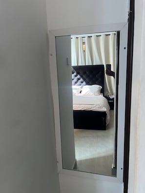 A bedroom with a bed, a nightstand, and a mirror reflecting the room. - New Listing (Accra)