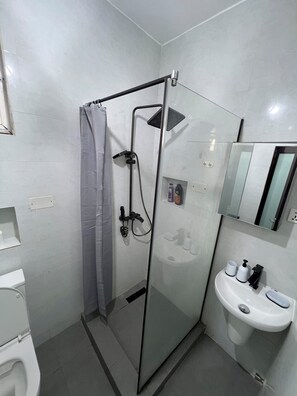 A modern bathroom with a glass-enclosed shower, a white sink, and a mirror above it. - New Listing (Accra)