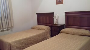 Un dormitorio con dos camas individuales, una mesita de noche con lámpara y una ventana con persianas.