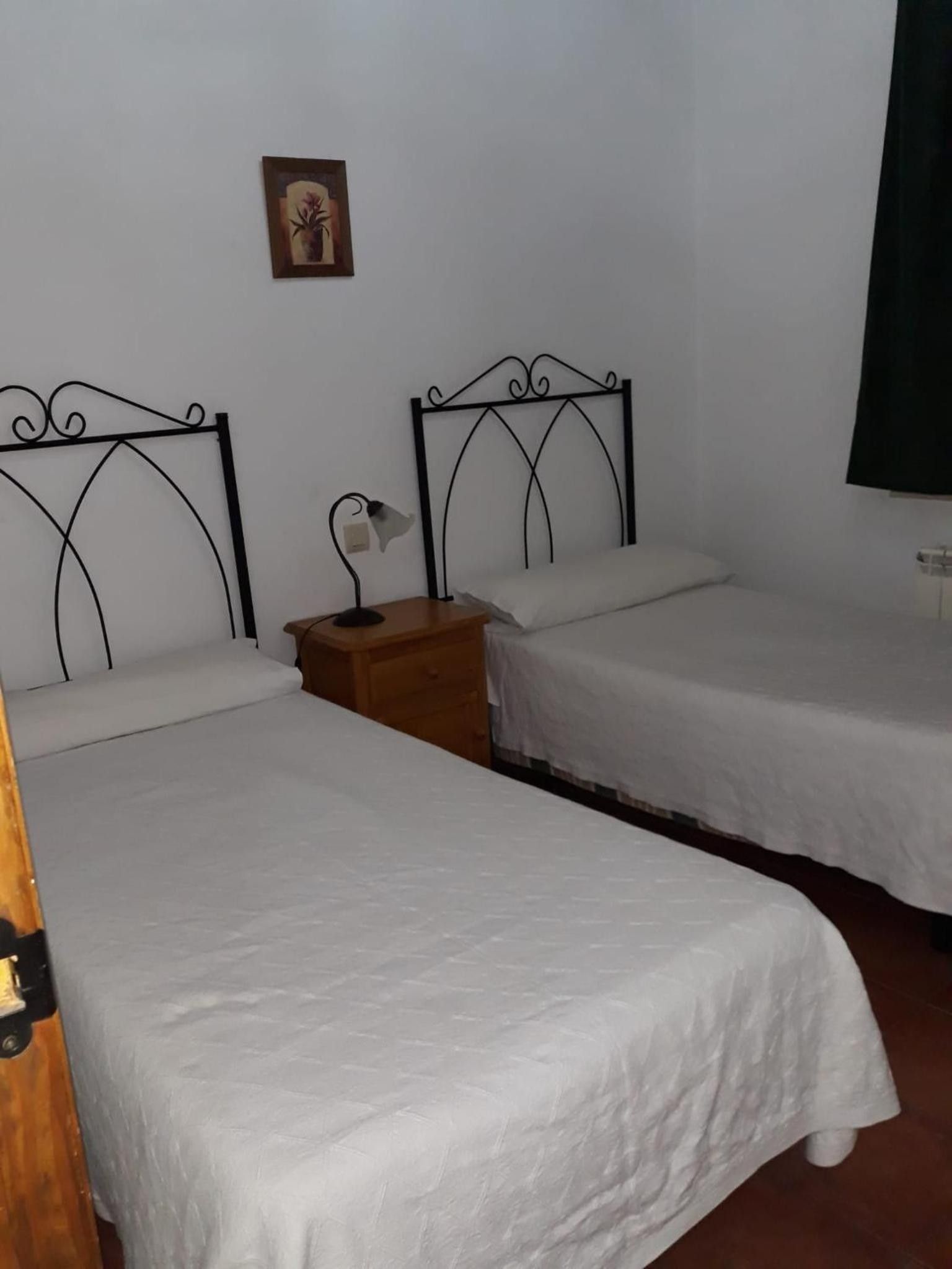 Una habitación con dos camas individuales, una mesita de noche con lámpara y un cuadro pequeño en la pared.