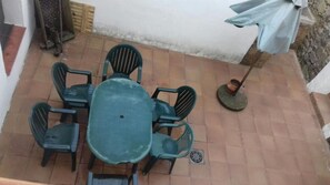 Un patio con una mesa redonda y seis sillas, una sombrilla pequeña y un muro de ladrillo.
