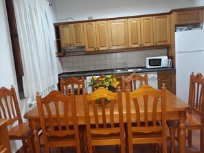 Un comedor con mesa y sillas de madera, un jarrón con flores y armarios de madera sobre la encimera.