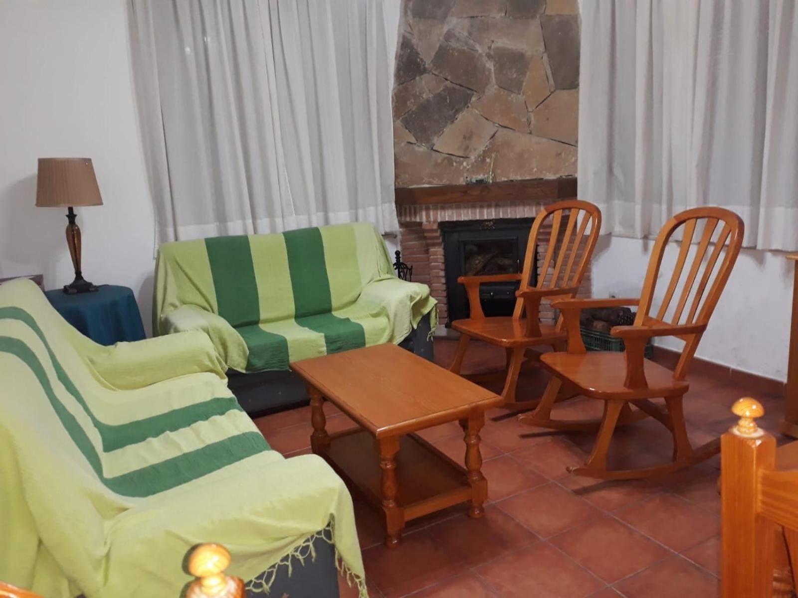 Una sala de estar con sofá, sillones, una mesa, una lámpara y una chimenea.
