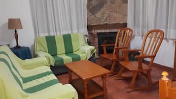 Una sala de estar con sofá, sillones, una mesa, una lámpara y una chimenea.