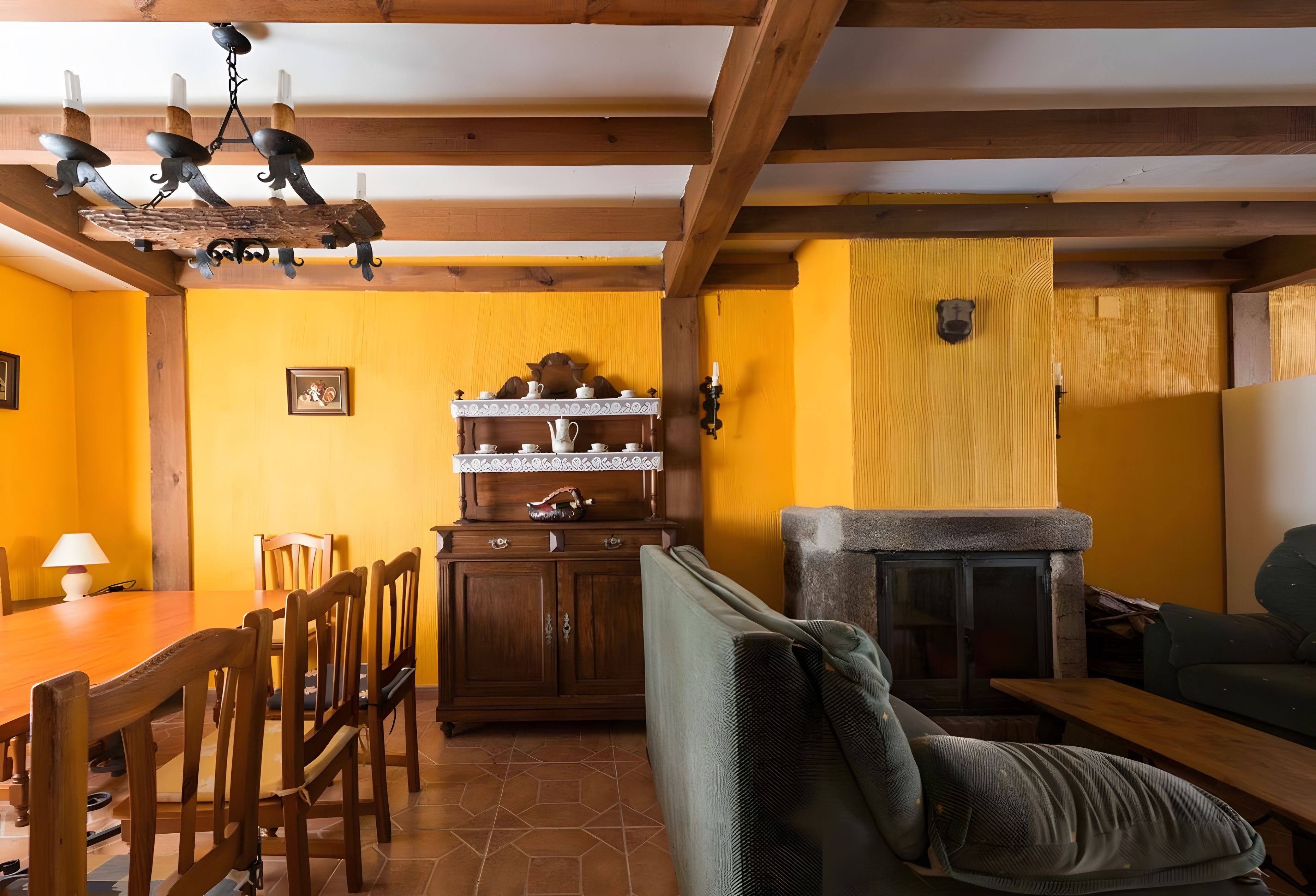 A dining area with wooden chairs and a table, a wooden cabinet with dishes, and a stone fireplace.