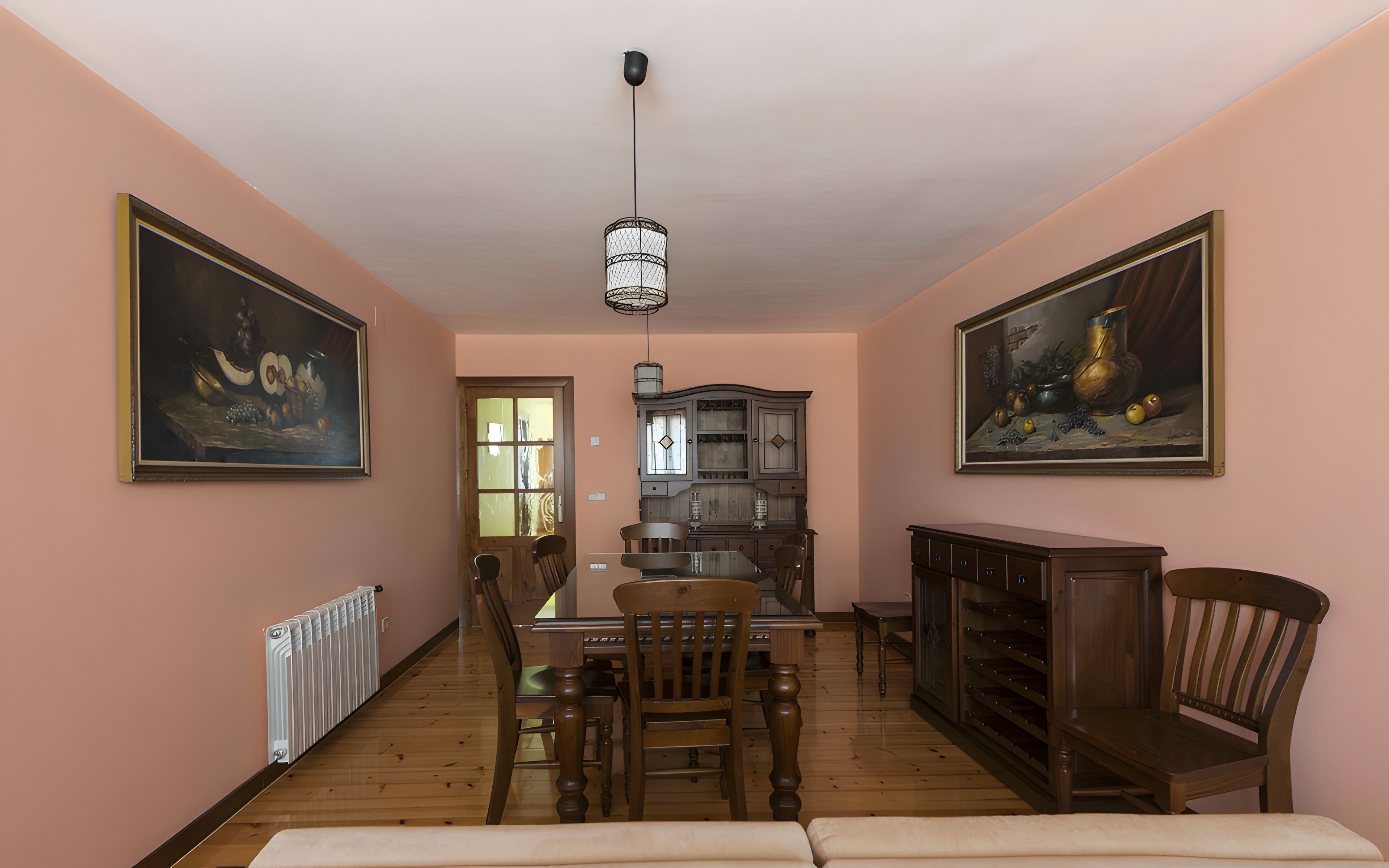 A dining area with a table, chairs, a hanging light fixture, and two framed paintings on the walls.
