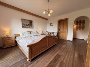 A bedroom with a wooden bed, bedside tables, a chandelier, a painting, and a wooden door. - New Listing (Kirchberg in Tirol)