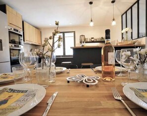A dining table set with plates, cutlery, and glasses, with a bottle of wine and decorative flowers. - New Listing (Goult)