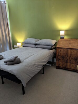A single bed with a white mattress and grey pillows, a bedside table with a lamp, and a wooden chest of drawers. - Quiet 2 bed house in Ramsgate. (Ramsgate)