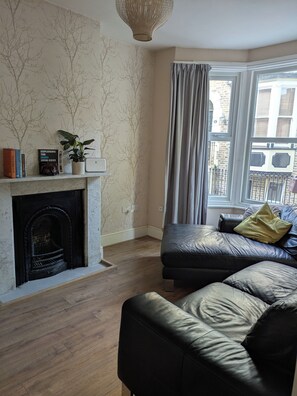 A living room with a fireplace, a sofa, a potted plant, and a window with curtains. - Quiet 2 bed house in Ramsgate. (Ramsgate)