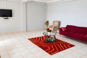 A modern living room with a flat-screen TV, a red sofa, a beige armchair, and a glass coffee table with a red rug. - Central 3BR Escape behind West Hills Mall (Mile 11)