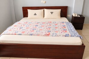 A bed with a patterned bedspread, two pillows, a wooden headboard, a nightstand with a phone, and a drawer. - Central 3BR Escape behind West Hills Mall (Mile 11)