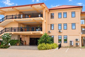 A multi-story hotel with balconies, air conditioning units, and a paved entrance area. - Central 3BR Escape behind West Hills Mall (Mile 11)