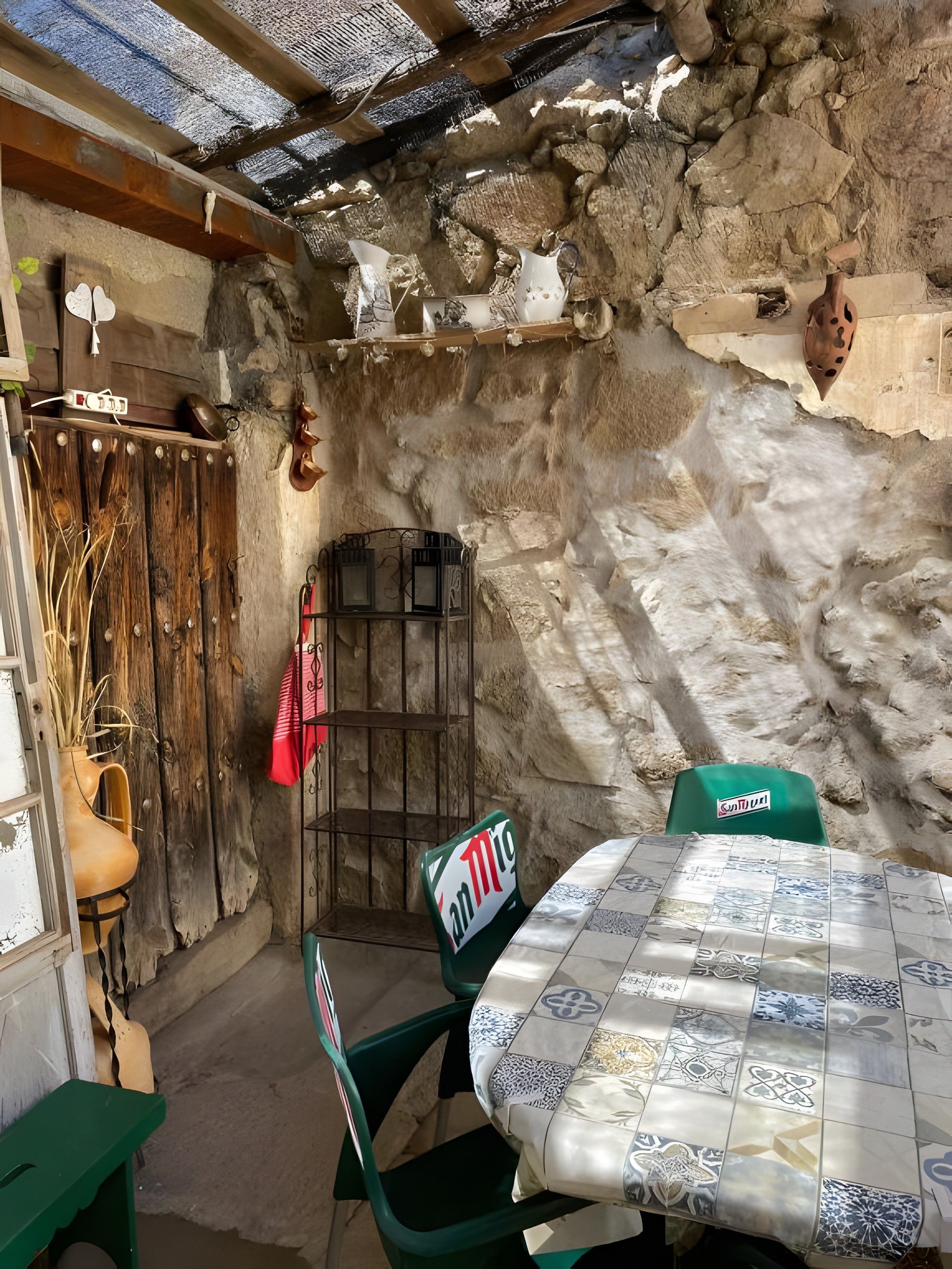 A rustic outdoor seating area with a stone wall, a wooden gate, and a table with a patterned tablecloth.