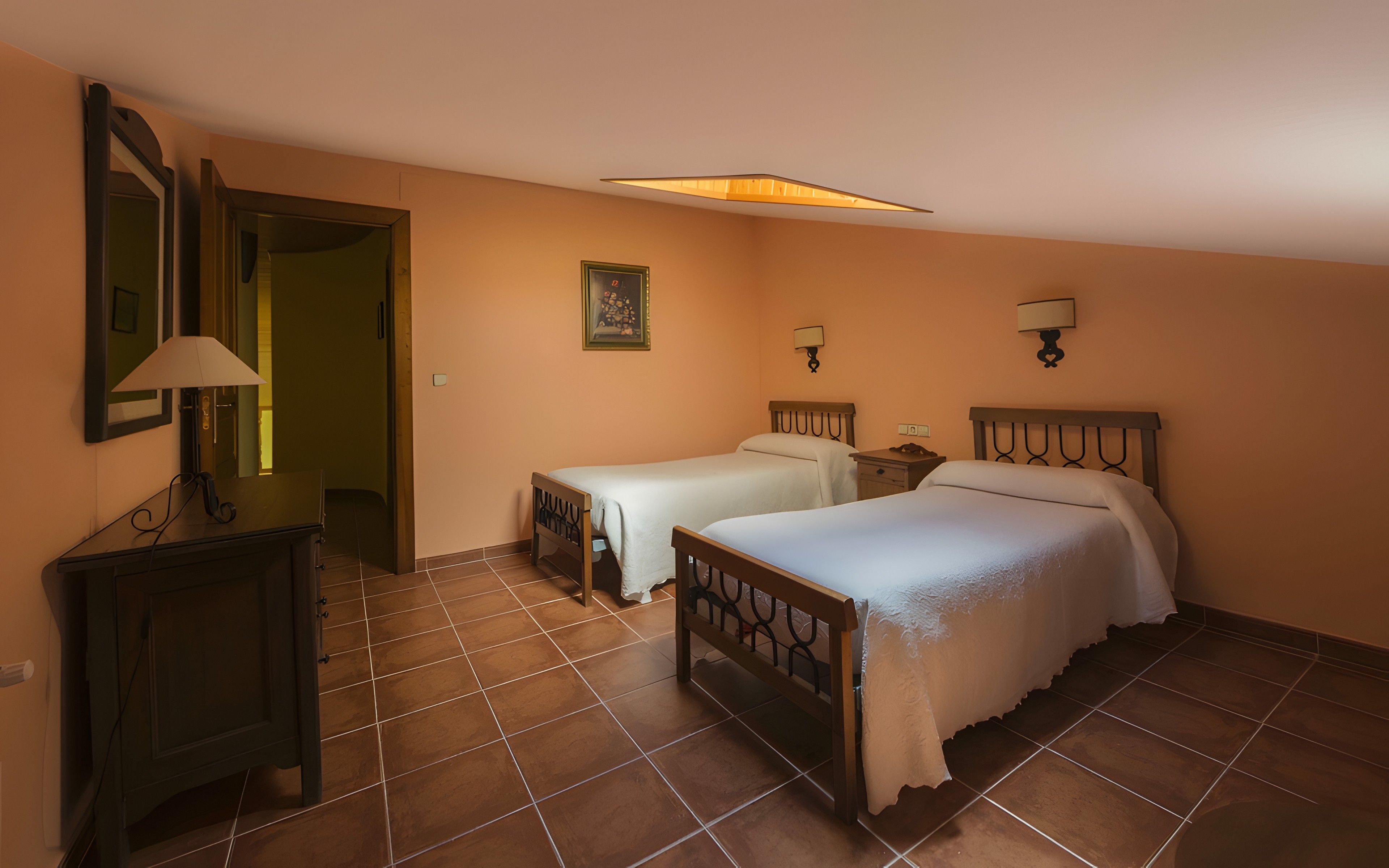 A hotel room with two beds, a nightstand, a lamp, a mirror, and a painting on the wall.