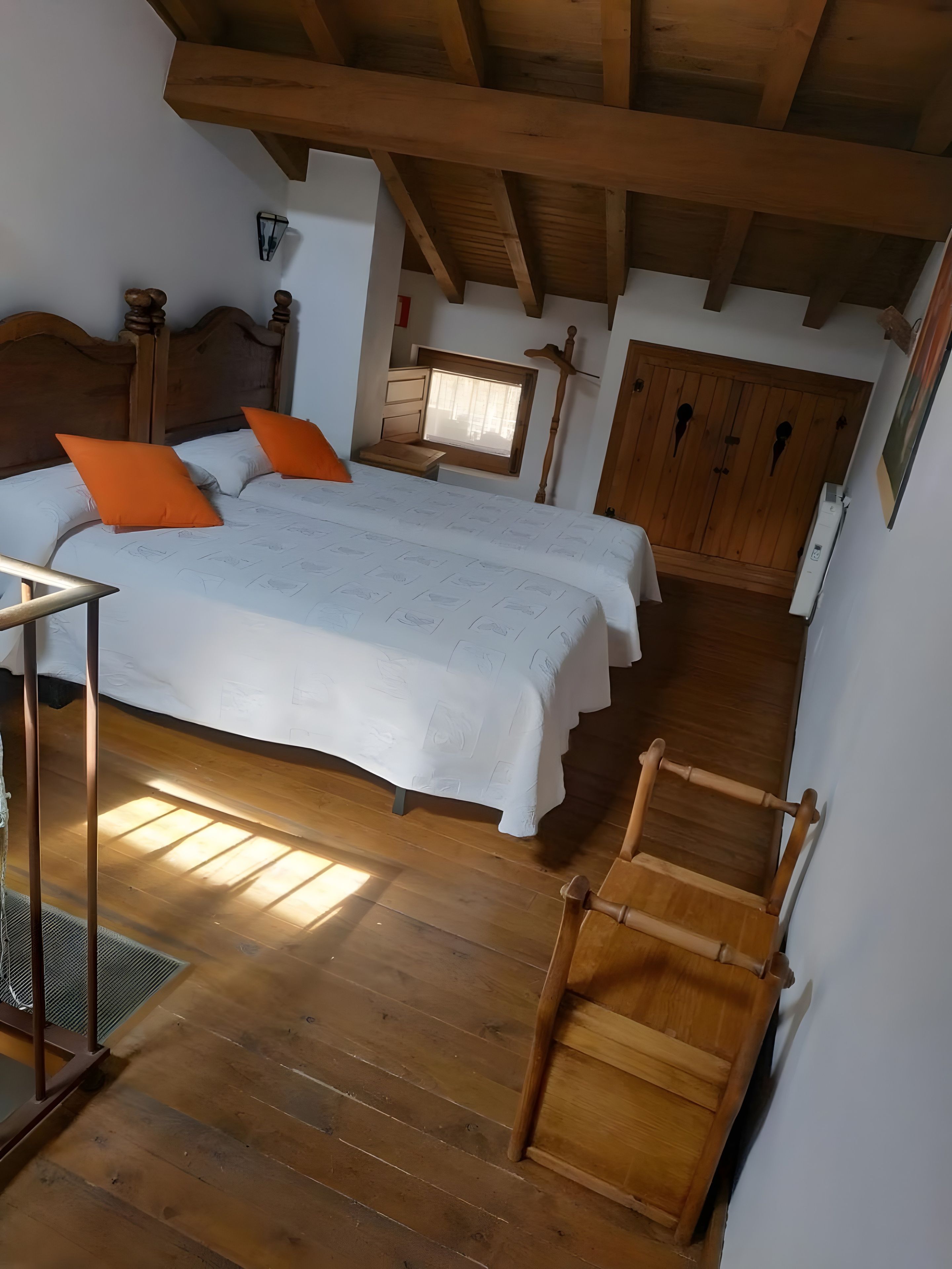 A bedroom with a wooden bed, a window, a wooden wardrobe, and a wooden chair.