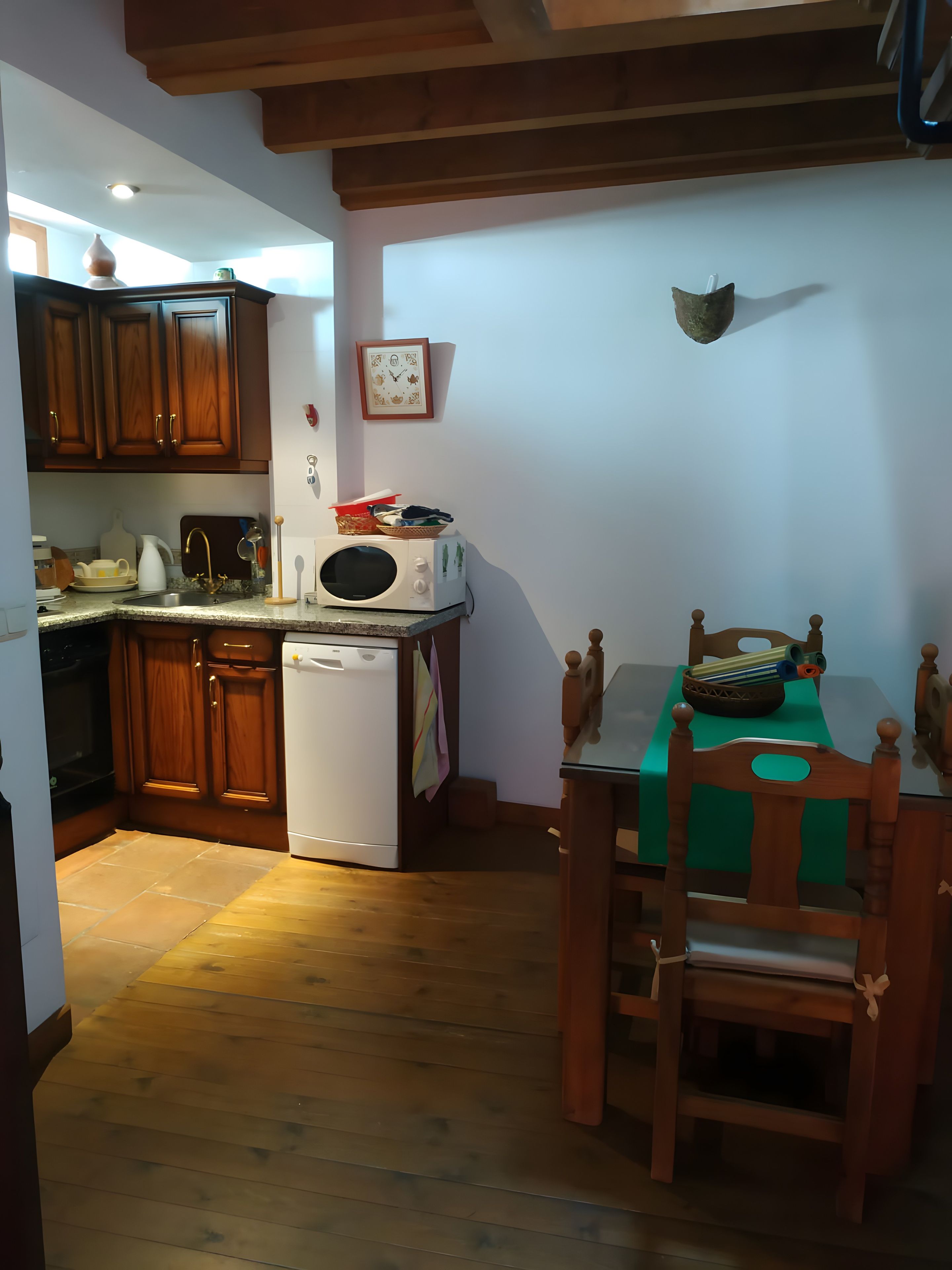 A compact kitchen with wooden cabinets, a white microwave, and a dining table with chairs.