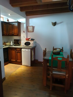 A compact kitchen with wooden cabinets, a white microwave, and a dining table with chairs. - Country House 'Casa Rural El Zapatero De Sexifirmo' with Balcony (Piedrahíta)