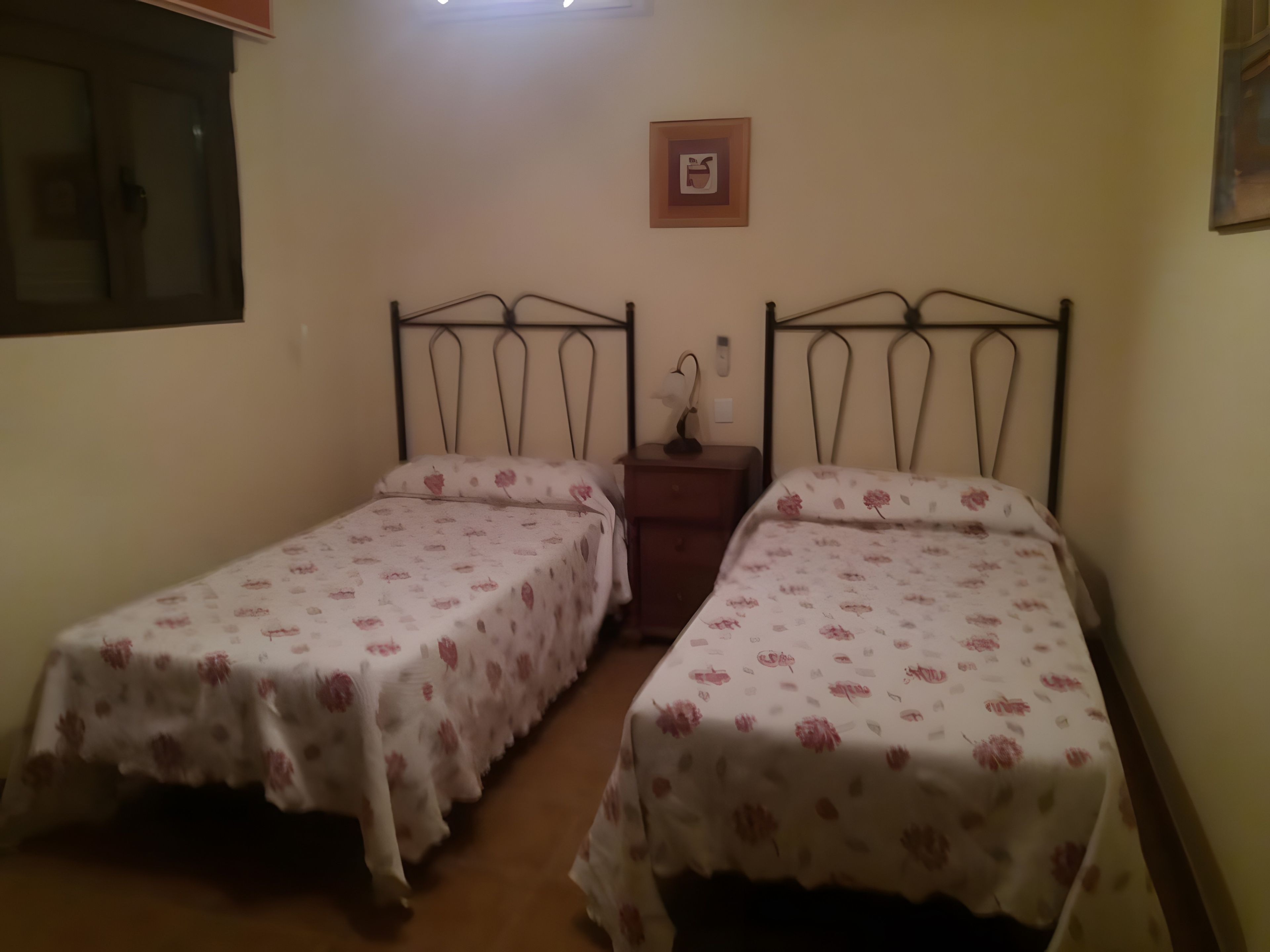 Une chambre avec deux lits simples, chacun recouvert d’une couvre-lit à motifs floraux. Il y a une table de chevet avec une lampe entre les deux lits.