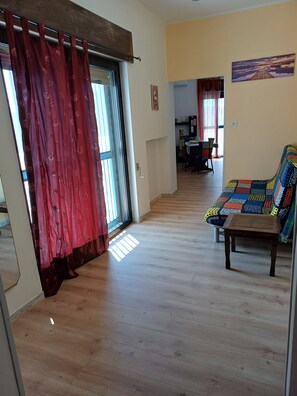 Ein Zimmer mit Holzboden, einem Sofa mit bunter Steppdecke, einem Essbereich mit Stühlen und Tisch sowie einem Gemälde an der Wand.