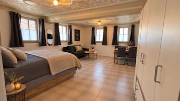 A hotel room with a bed, a sofa, a dining table with chairs, and a large wardrobe.