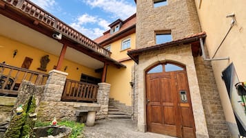A stone building with a wooden door, a balcony, and a stone staircase leading to a porch.