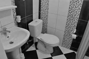 A bathroom with a white sink, toilet, and black and white checkered floor. - Durak villa pansiyon (Bodrum)