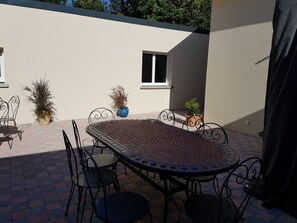 Eine Terrasse im Freien mit einem runden Tisch, Stühlen, Blumentöpfen und einem Fenster.