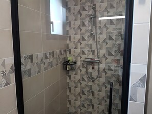 Eine Dusche mit einem geometrischen Fliesenmuster, einer Handbrause und einer Shampooflasche in einem Halter.