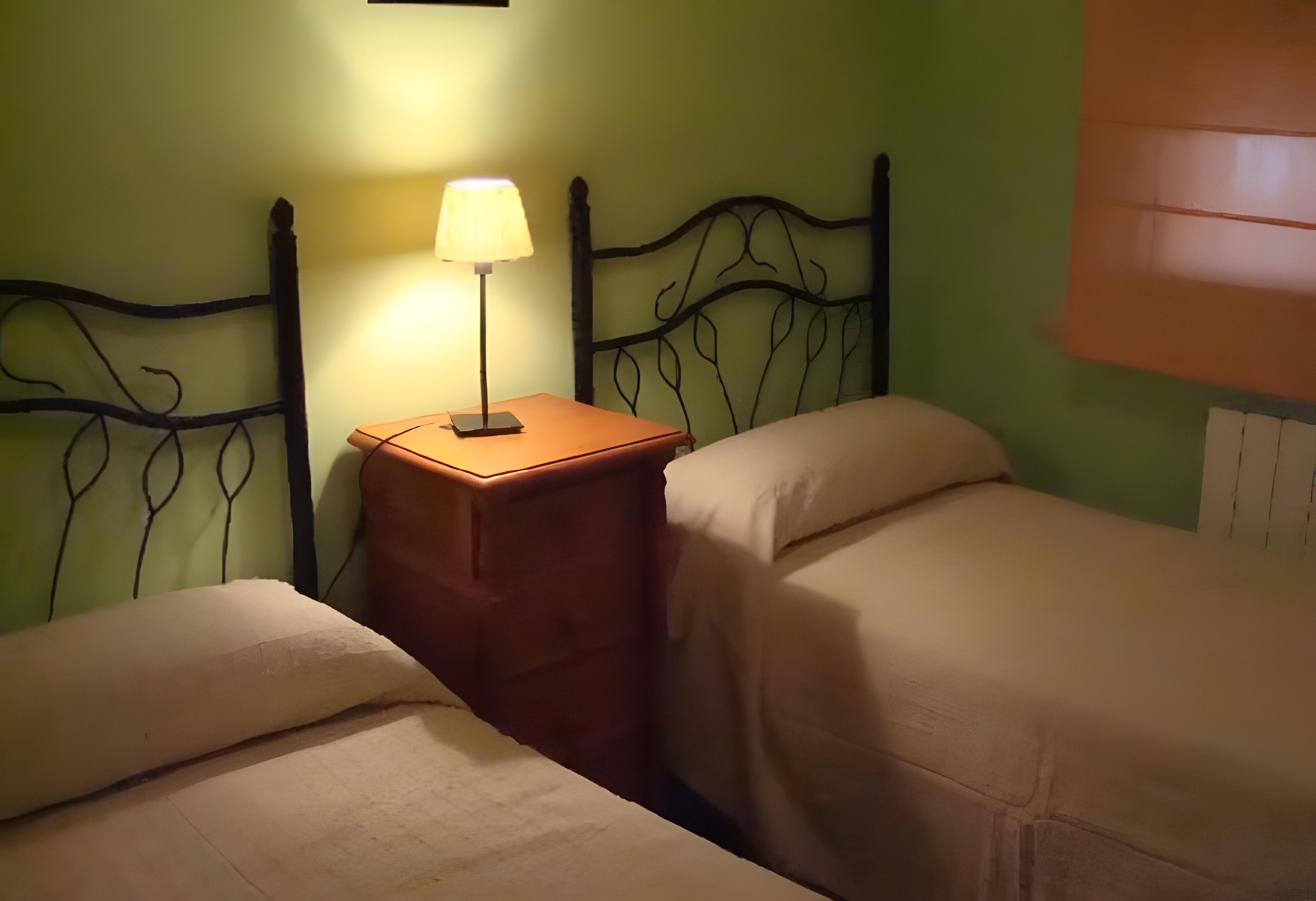 Una habitación con dos camas, una mesita de noche con lámpara y un cabecero metálico decorativo en la pared.