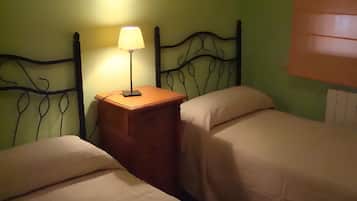 Una habitación con dos camas, una mesita de noche con lámpara y un cabecero metálico decorativo en la pared.