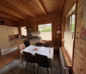 Ein gemütliches Blockhauszimmer mit Esstisch, Stühlen, einer Küchenzeile und einem großen Fenster.