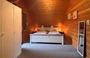 Ein Schlafzimmer mit Holzboden, einem Bett mit zwei Kissen, Nachttischen mit Lampen und einem Kleiderschrank.