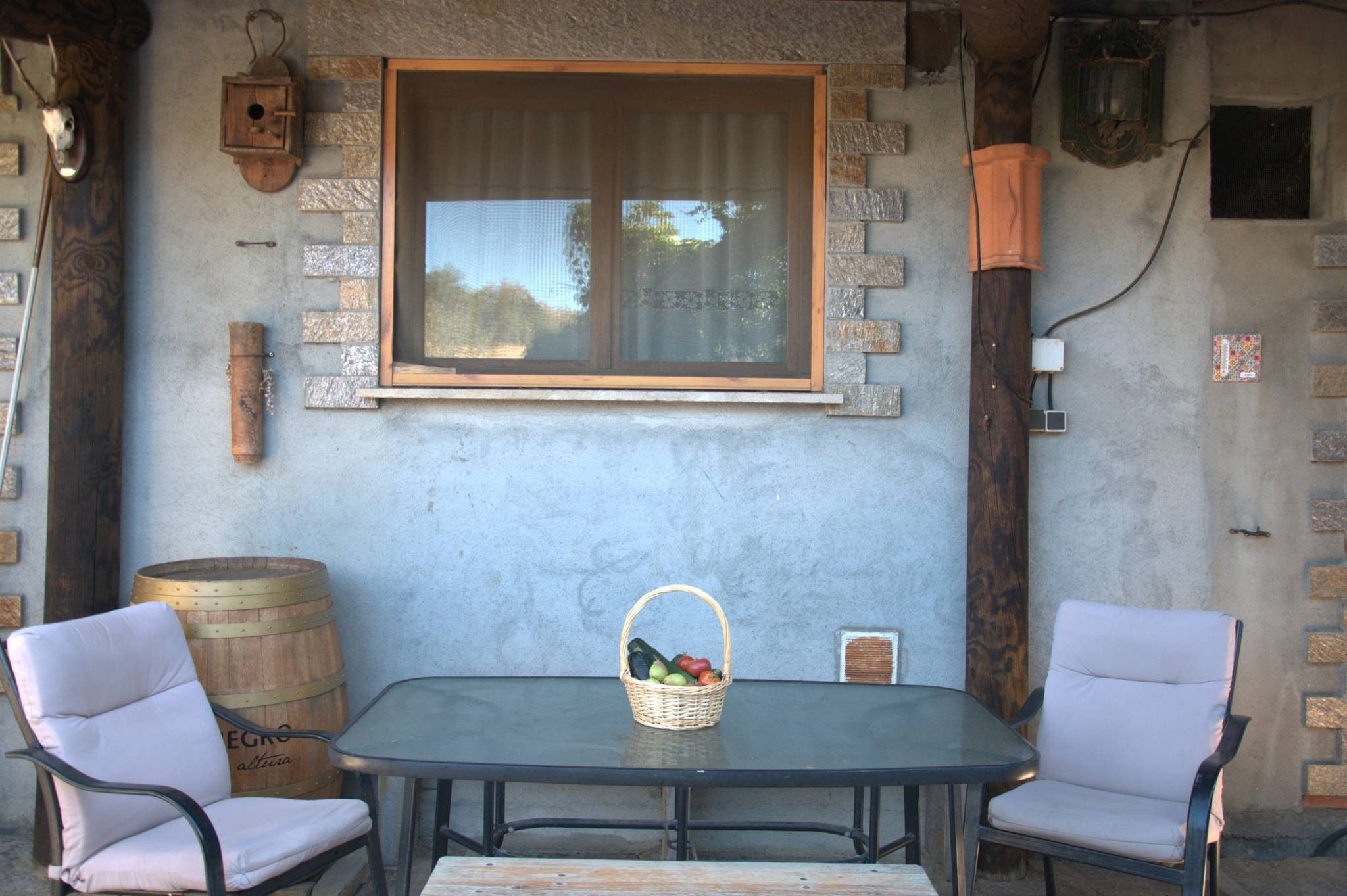 Une table avec deux chaises, un panier de fruits et un mur de pierre rustique avec une fenêtre.