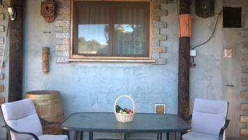 Une table avec deux chaises, un panier de fruits et un mur de pierre rustique avec une fenêtre.