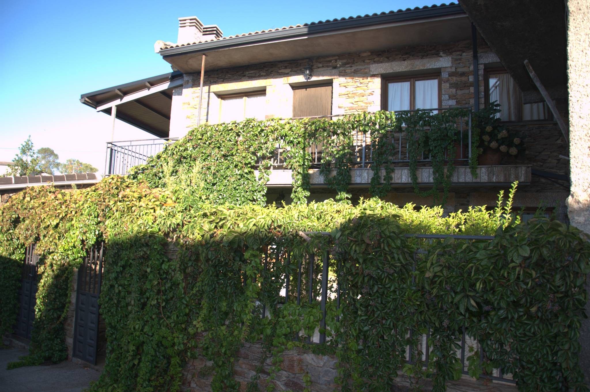 Une maison avec une façade en pierre, un balcon orné de plantes et un ciel dégagé.