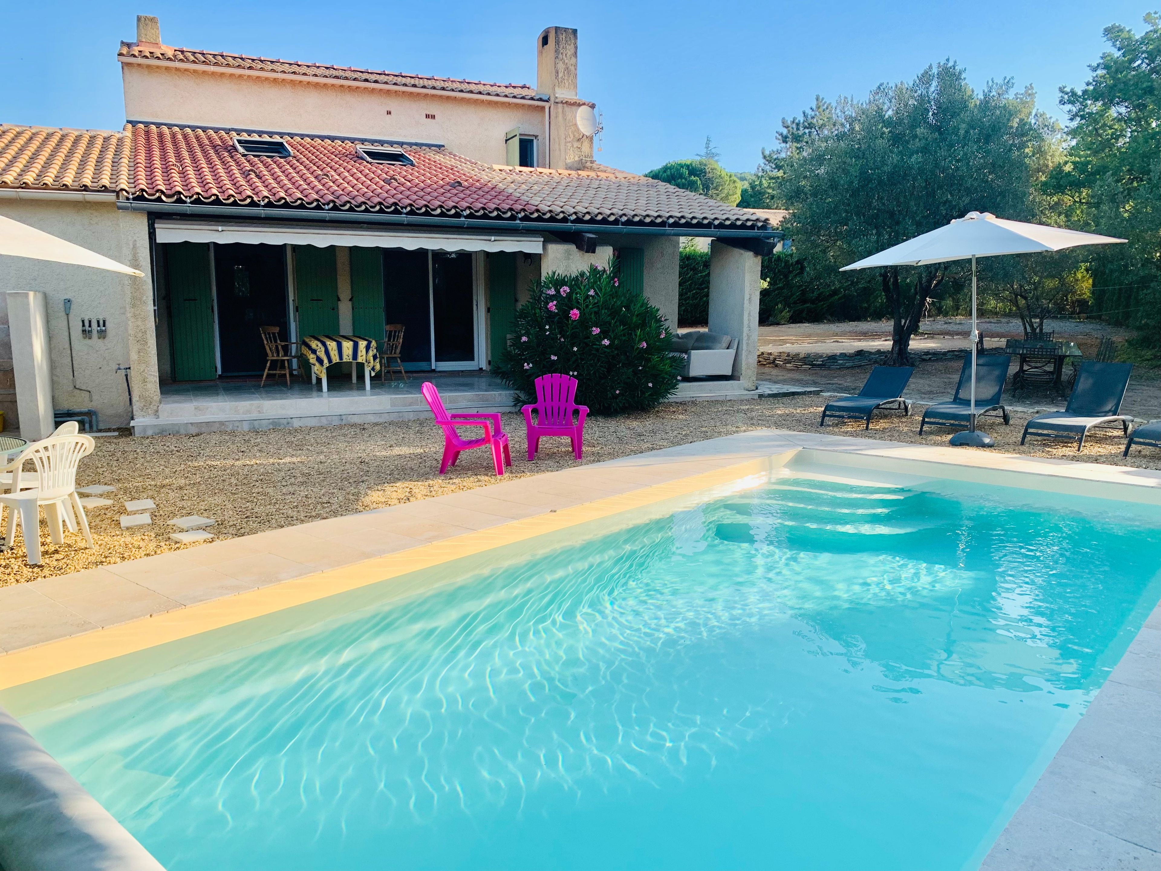 Une piscine avec une terrasse carrelée, un patio couvert avec des meubles d’extérieur et un bâtiment doté d’un toit carrelé.