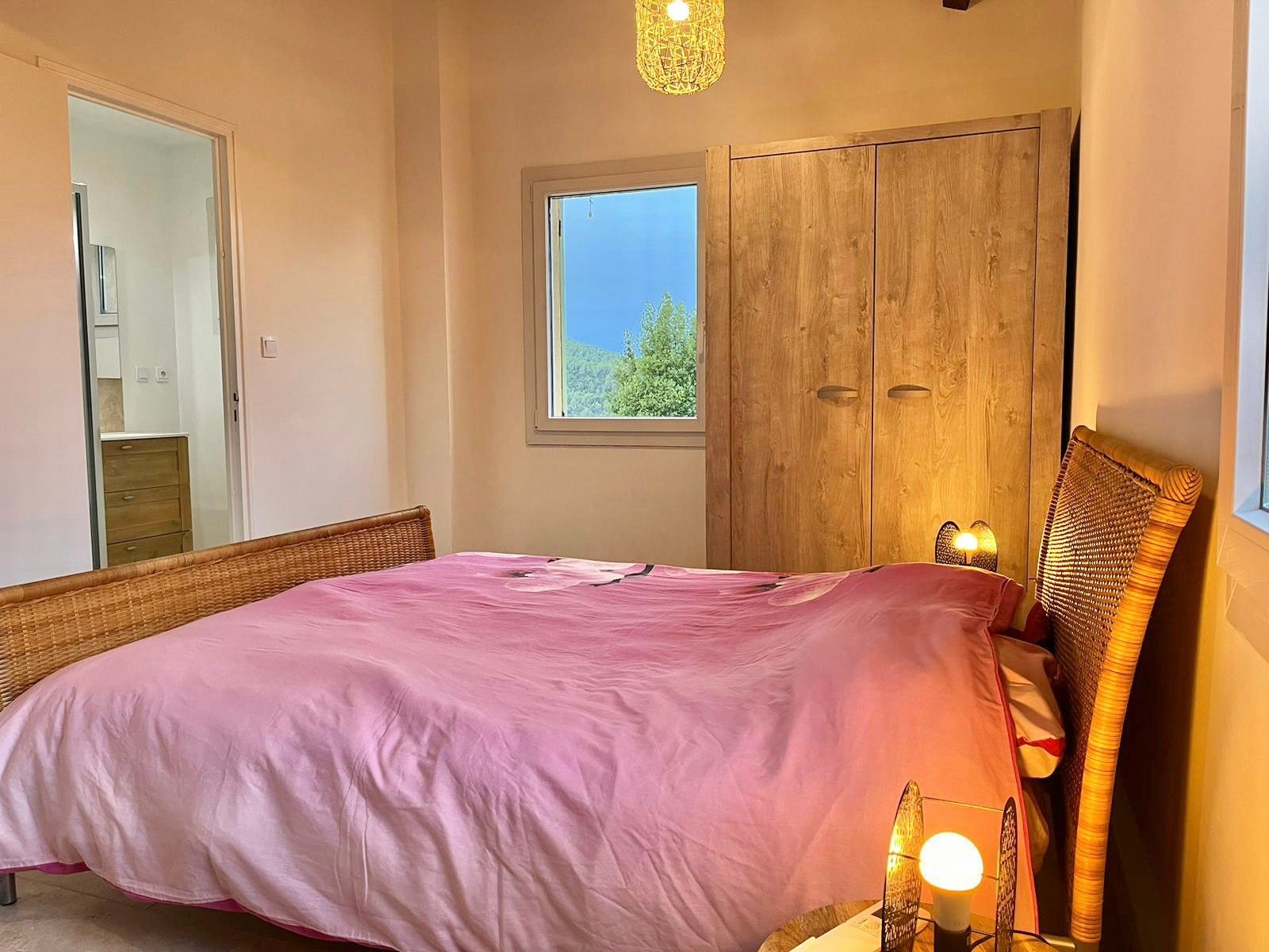 Une chambre à coucher avec un lit, une armoire, une fenêtre donnant sur un beau paysage et un luminaire suspendu.