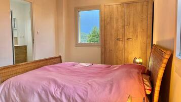 Une chambre à coucher avec un lit, une armoire, une fenêtre donnant sur un beau paysage et un luminaire suspendu.