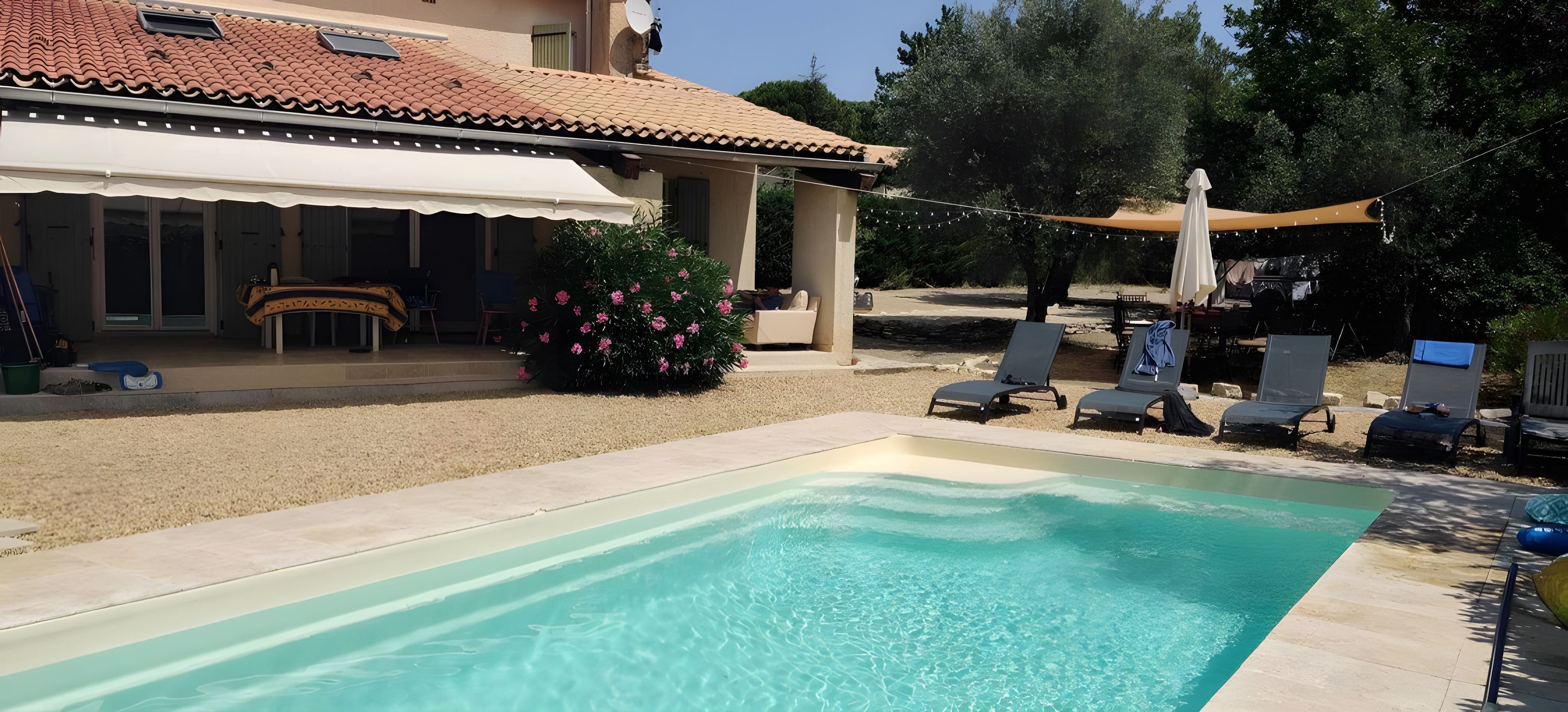 Une piscine avec des chaises longues, un patio couvert et un jardin fleuri.
