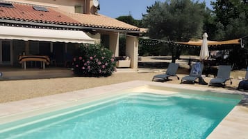Une piscine avec des chaises longues, un patio couvert et un jardin fleuri.