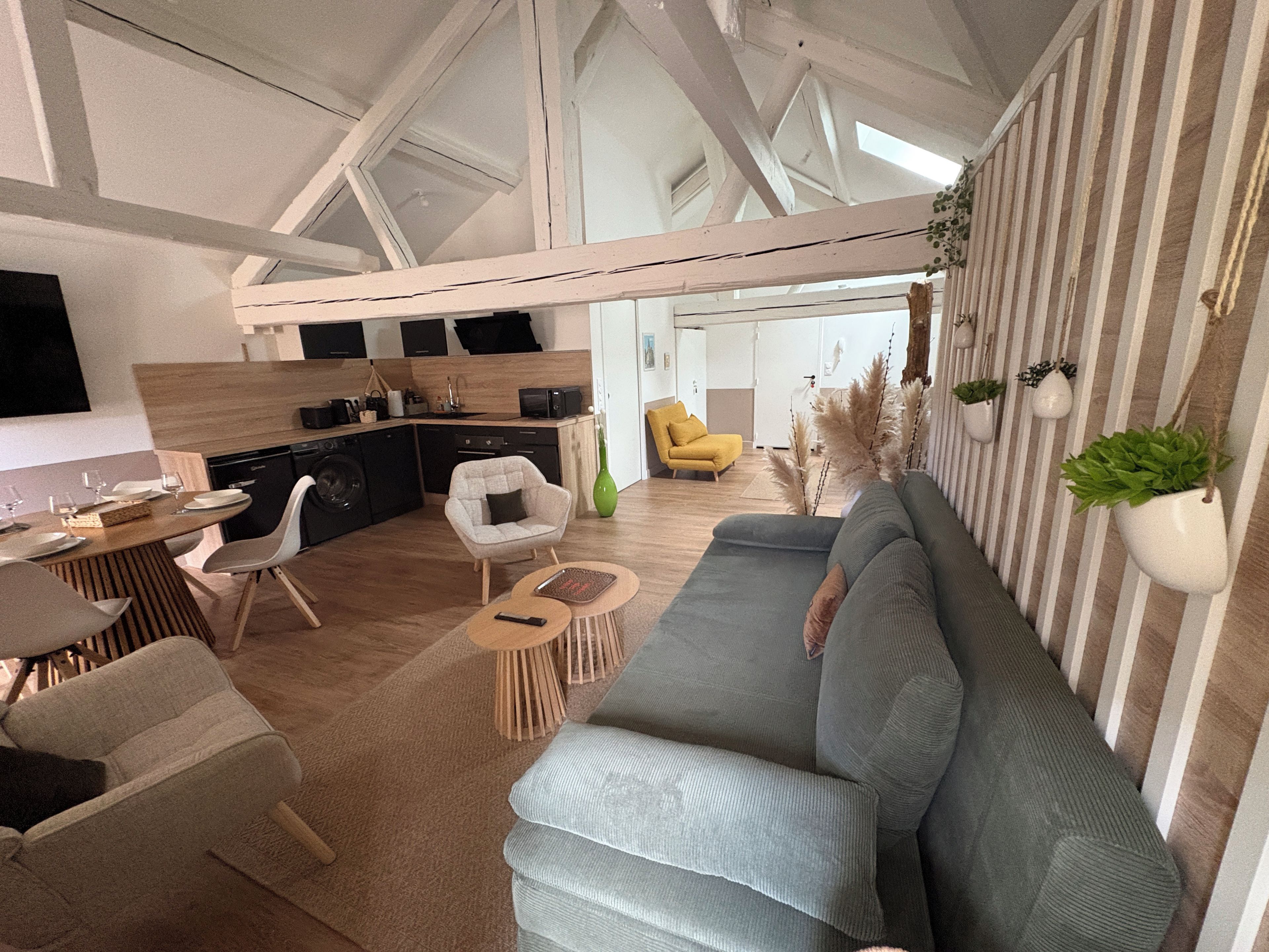 Un salon moderne avec un canapé, des fauteuils, un coin repas et une cuisine en arrière-plan.