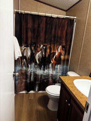 Un baño con cortina de ducha decorada con caballos, un inodoro y un lavabo con encimera de granito.