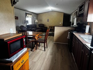 Cocina compacta con microondas, mesa de madera, sillas y refrigerador.